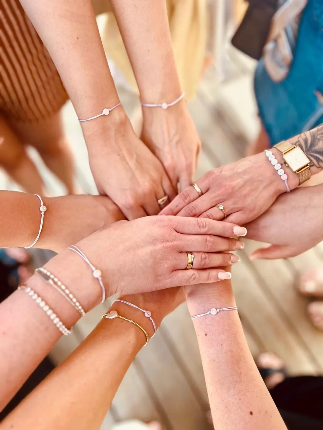 Viele Hände mit selbstgemachten Perlenarmbändern übereinander