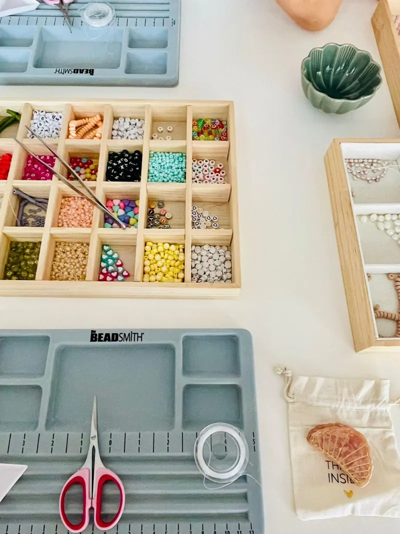 Sortierbox mit bunten Perlen, Schere und Perlenbrett von oben
